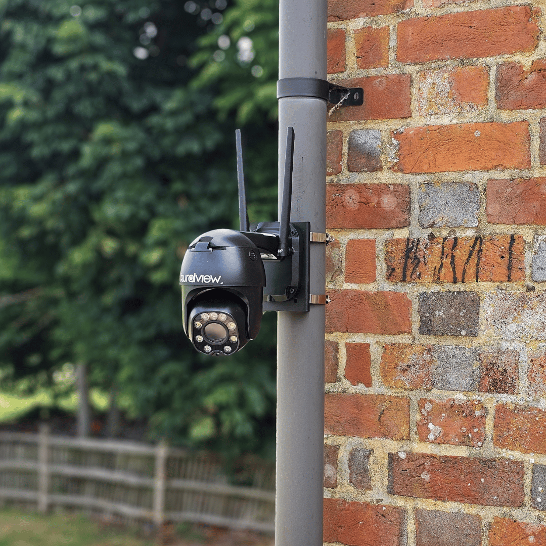 RuralView 360 Mini camera mounted beside a brick wall overlooking a rural yard.